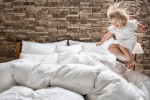 Vysmiate dieťa skáče do mäkkých páperových perín Atelliere – prirodzený komfort, ľahkosť a radosť z dotyku prírody.